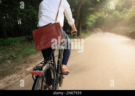Vue arrière de l'employé de sexe masculin dans des vêtements élégants, vélo à vélo pour travailler le matin ensoleillé. Vue rognée d'un homme méconnaissable avec porte-documents en cuir Banque D'Images