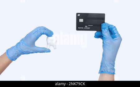 La main de dentiste femelle dans des gants bleus tient le modèle de dent de dentiste et la carte de crédit. Arrière-plan clair. Concept du coût du traitement dentaire Banque D'Images
