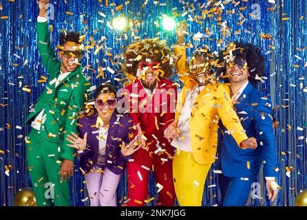 Groupe d'amis heureux et excités dans des costumes colorés et funky s'amusant à la soirée disco Banque D'Images
