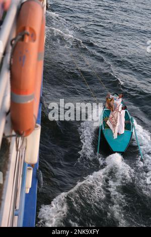 Des hommes qui vendent des bijoux touristiques et des souvenirs textiles à partir d'un petit bateau attaché à un bateau de croisière sur le Nil Banque D'Images