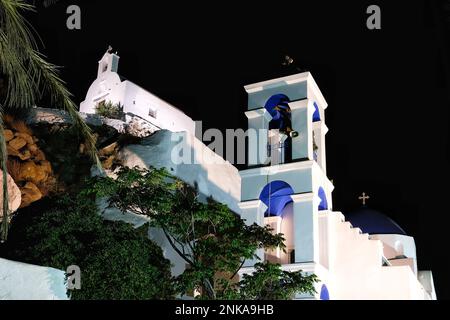 L'église orthodoxe blanchie à la chaux illuminée de Panagia Gremniotissa à iOS Grèce, entourée de palmiers la nuit Banque D'Images