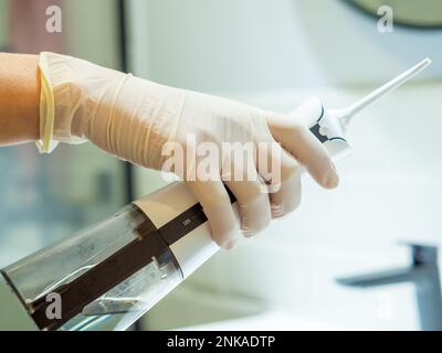 Main du dentiste montrant comment utiliser un démousseur d'eau dentaire domestique pour un nettoyage en profondeur à la maison Banque D'Images