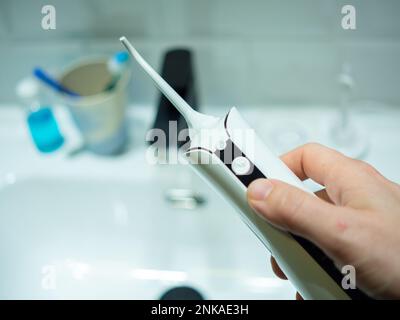 jeune homme main tenant une flasseur d'eau dentaire domestique devant un lavabo de salle de bains Banque D'Images