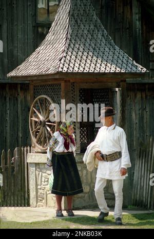 Straja, Comté de Suceava, Roumanie, 1998. Couple de personnes âgées portant des vêtements traditionnels près d'un puits d'eau avec roue et toit de bardeaux en bois. Banque D'Images