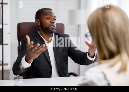 Embauche, entrevue. Un patron d'entreprise afro-américain d'âge moyen tient un entretien d'emploi dans un bureau lumineux. Il regarde le CV, il n'aime pas Banque D'Images