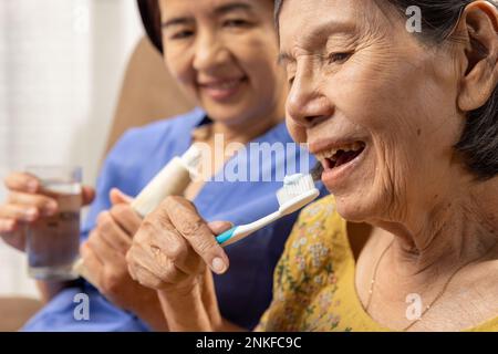 Le soignant prend soin de femme asiatique âgée tout en se brossant les dents. Banque D'Images