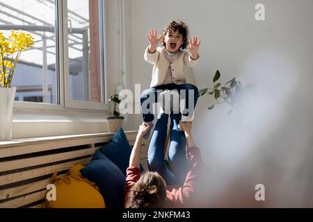 Mère fille volante sur les jambes allongé sur le canapé Banque D'Images