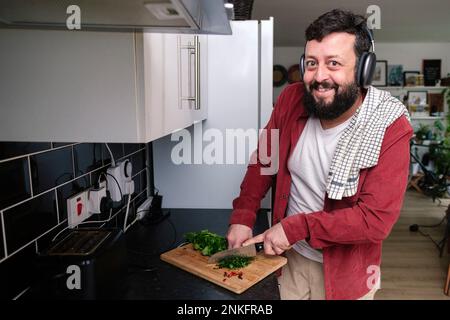 Heureux homme mature portant un casque coupant des légumes dans la cuisine Banque D'Images