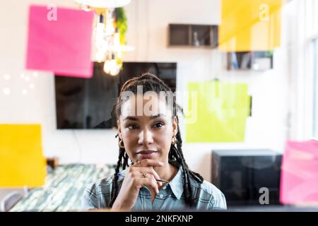 Femme d'affaires bien réfléchie lisant des notes adhésives sur le verre dans le bureau Banque D'Images