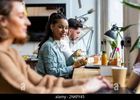 Femme d'affaires souriante qui mange de la salade au bureau Banque D'Images