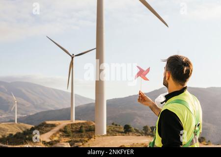 Technicien tenant le jouet de roue dentée devant l'éolienne Banque D'Images