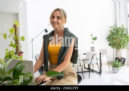 Travailleur indépendant souriant avec ordinateur portable travaillant à la maison Banque D'Images