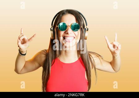 Jeune femme avec un casque faisant signe de corne sur fond jaune Banque D'Images