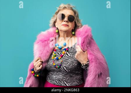 Femme aînée souriante portant un manteau de fourrure sur fond turquoise Banque D'Images