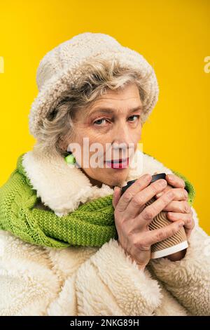 Femme âgée avec une tasse à café jetable sur fond coloré Banque D'Images