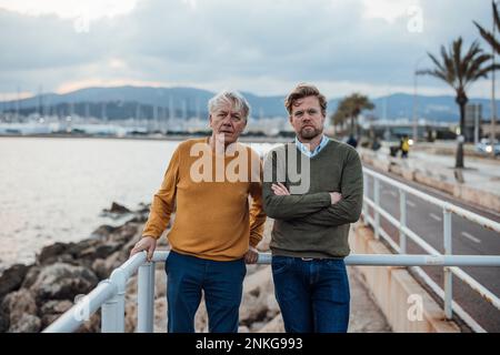 Homme âgé avec son fils s'inclinant sur une rampe au coucher du soleil Banque D'Images