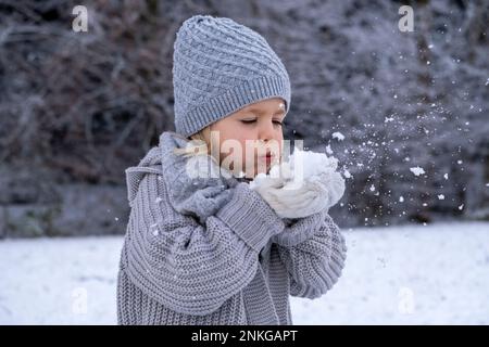 Fille joueur dans des vêtements chauds soufflant de neige Banque D'Images