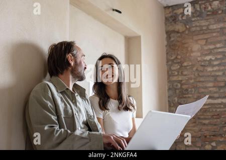 Femme et homme heureux assis avec un ordinateur portable à la maison Banque D'Images