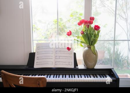 Piano avec bouquet de tulipes et feuilles de musique devant la fenêtre à la maison Banque D'Images