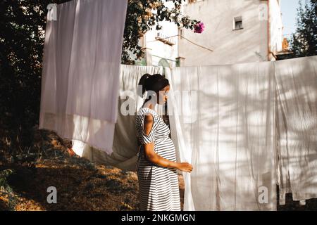 Femme enceinte qui pendait un drap blanc dans l'arrière-cour Banque D'Images