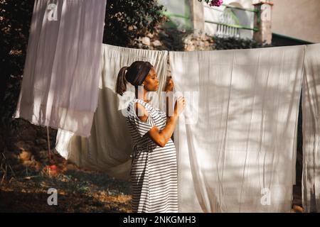 Femme enceinte qui pendait un drap blanc à l'arrière-cour Banque D'Images