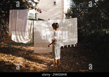 Femme enceinte qui pendait un drap blanc à l'arrière-cour dans le jardin Banque D'Images