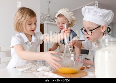 Fille avec des frères mélangeant des œufs dans un bol à la cuisine Banque D'Images