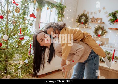 Bonne mère qui donne une promenade en porcgyback à sa fille à Noël Banque D'Images