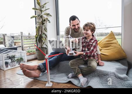 Père et fils jouant avec le modèle d'éolienne assis à la maison Banque D'Images