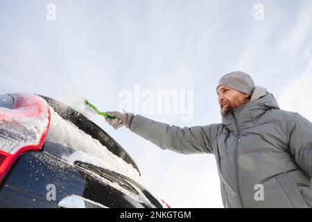 Homme portant un chapeau en tricot qui se brosse la neige de la voiture Banque D'Images