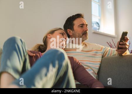 Homme utilisant un smartphone assis avec une femme à la maison Banque D'Images