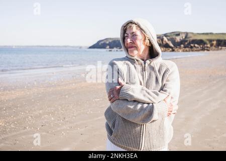 Femme sénior réfléchie avec les bras croisés à la plage Banque D'Images