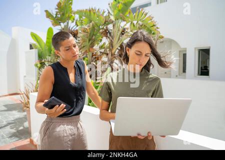 Femme d'affaires travaillant sur un ordinateur portable par un collègue tenant un smartphone Banque D'Images