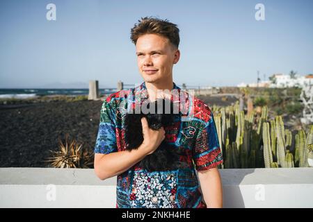 Jeune homme souriant debout avec un chien noir par beau temps Banque D'Images