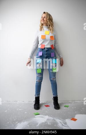 Femme souriante avec des notes adhésives colorées sur le corps debout devant le mur Banque D'Images