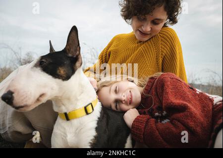 La fille se détend sur les genoux de sa mère avec le chien Bull Terrier Banque D'Images