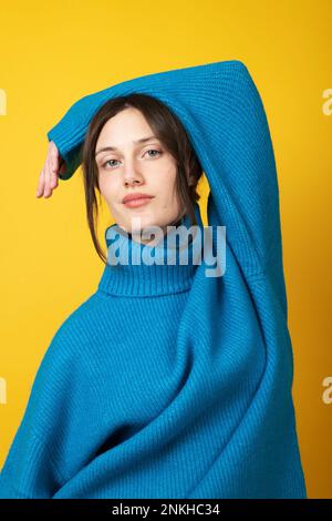 Jeune femme confiante portant un col de cygne bleu sur fond jaune Banque D'Images