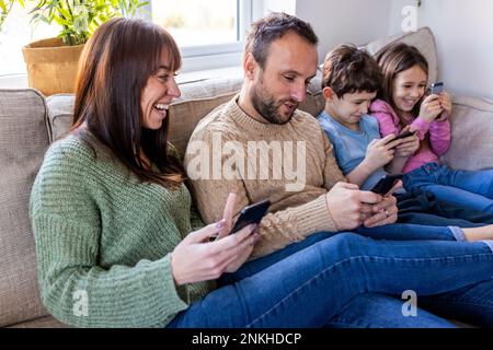 Une femme heureuse avec sa famille utilisant un téléphone portable sur son canapé à la maison Banque D'Images