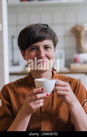 Femme mûre souriante tenant une tasse de café à la maison Banque D'Images