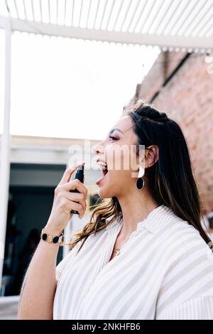 Femme utilisant le spray buccal sur le toit Banque D'Images