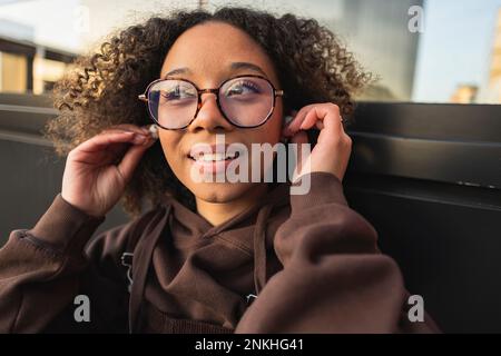 Jeune femme aux cheveux bouclés portant des écouteurs intra-auriculaires sans fil Banque D'Images