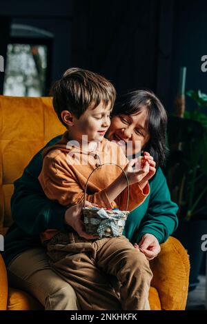 Grand-mère heureuse avec petit-fils tenant des œufs de chocolat de Pâques assis sur un fauteuil Banque D'Images