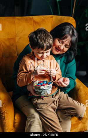 Grand-mère heureuse avec petit-fils contenant un panier d'œufs de chocolat de Pâques Banque D'Images