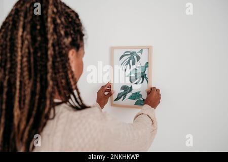 Femme mûre qui pendait le cadre d'image sur le mur à la maison Banque D'Images