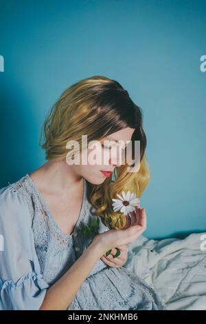 Belle femme blonde regardant la fleur près du mur bleu Banque D'Images