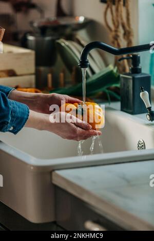 Mains de femme lavant de la tomate fraîche sous le robinet dans la cuisine Banque D'Images