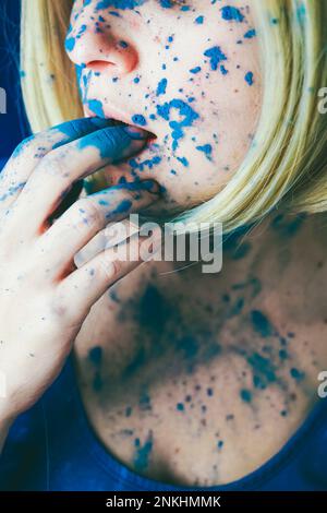 Femme mord les doigts recouverts de peinture bleue Banque D'Images