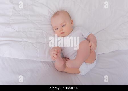 bébé aux yeux bleus dans un body blanc se trouve dans un berceau et regarde la caméra. Photo de haute qualité Banque D'Images