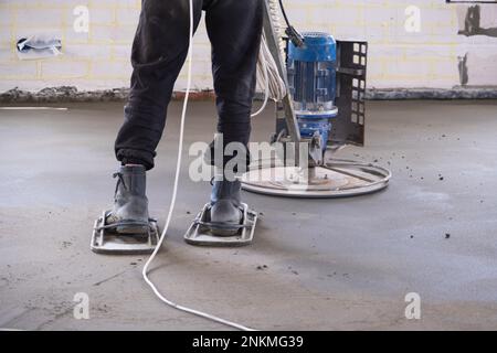 Rembaryage et meulage d'une table semi-sèche sur sol par une machine équipée d'un disque rotatif pour la mise à niveau. Construction d'un plancher en béton dans la maison, un maître Banque D'Images