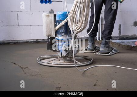 Rembaryage et meulage d'une table semi-sèche sur sol par une machine équipée d'un disque rotatif pour la mise à niveau. Construction d'un plancher en béton dans la maison, un maître Banque D'Images